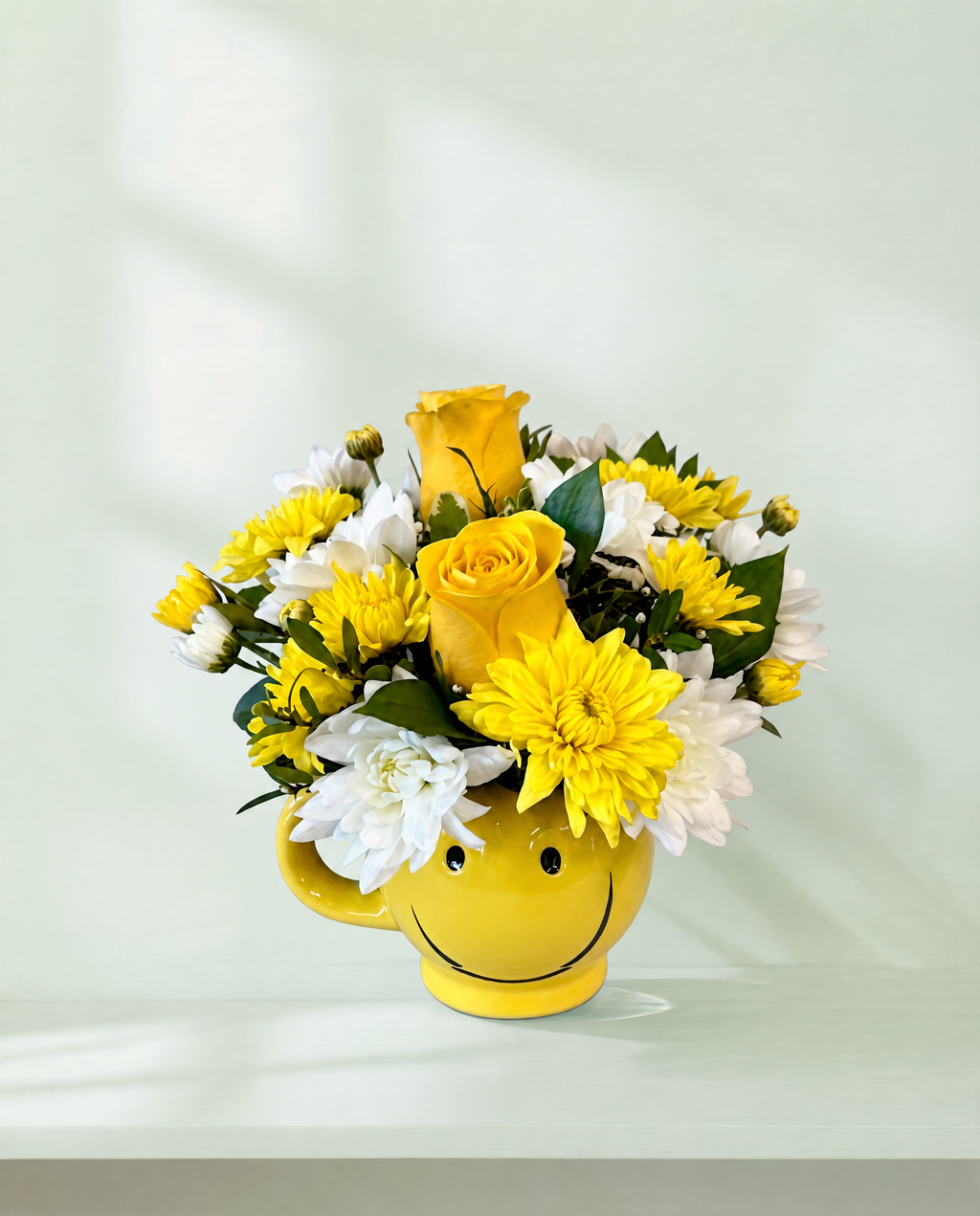 Lakewood Florist yellow smiley face mug filled with a cheerful arrangement of yellow roses and white chrysanthemums.