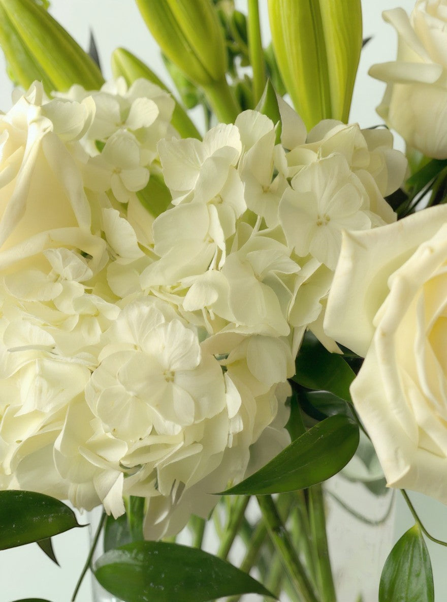 Lakewood Florist elegant white lilies, roses, and hydrangeas with lush greenery in a glass vase.